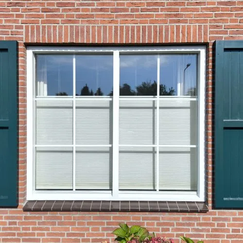 Wit raamkozijn met roedenverdeling en donkergroene luiken